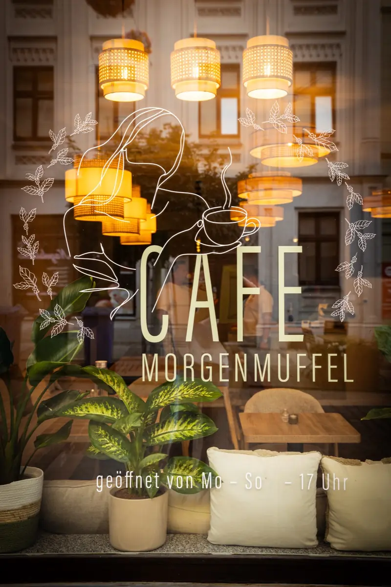 Schaufenster des Café Morgenmuffel mit Logo und leuchtenden Rattanlampen